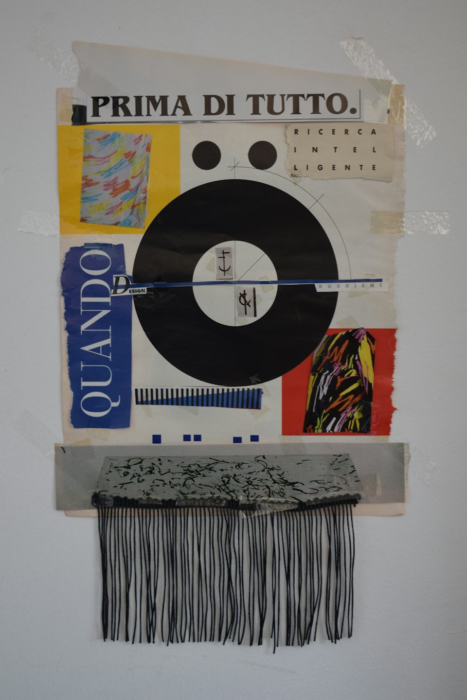 Collage aus Papierresten und Schnüren an einer Wand.