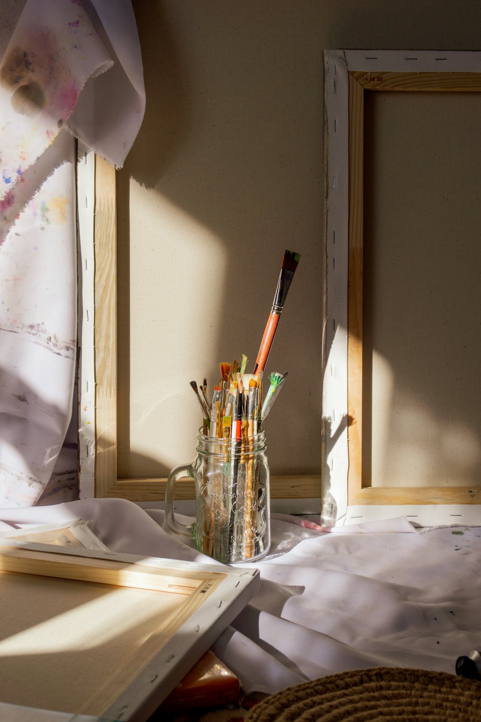 Leere Leinwände lehnen an einer Wand neben einem Pinselglas.